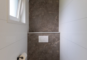 Bagno moderno e stretto con WC, finestra e parete in marmo al Wellness Cottage, De Thijmse Berg, Paesi Bassi.