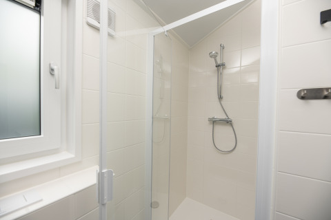 Modern shower cabin with glass door and white tiled walls at Doornenburg Lodge Comfort, Veluwepark de Bosgraaf.