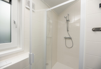 Modern shower cabin with glass door and white tiled walls at Doornenburg Lodge Comfort, Veluwepark de Bosgraaf.