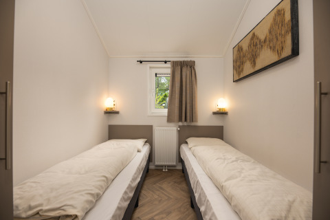 Tweepersoonskamer met eenvoudige inrichting, klein raam en verlichting bij Doornenburg Lodge Comfort, Veluwepark de Bosgraaf.