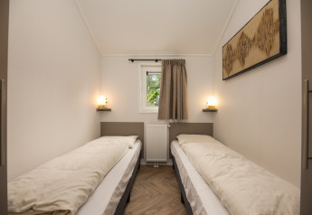 Dormitorio con dos camas individuales, ventana pequeña y luz suave en Doornenburg Lodge Comfort, Veluwepark de Bosgraaf.