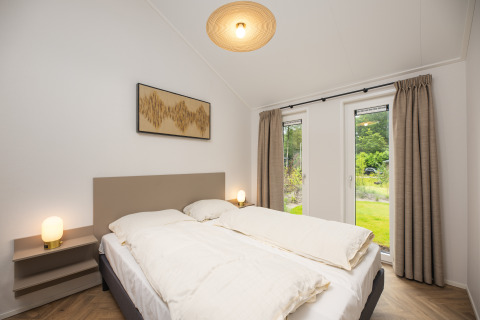 Camera moderna con letto matrimoniale, comodini e grandi finestre alla Doornenburg Lodge Comfort nei Paesi Bassi.