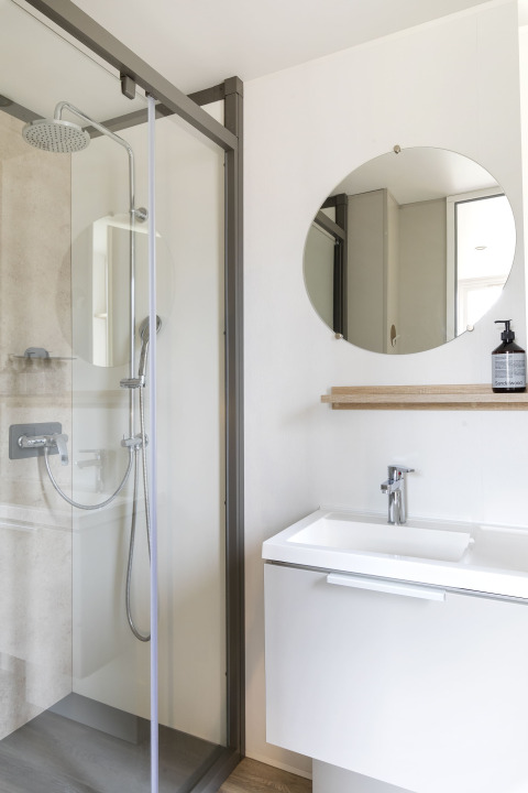 Bagno moderno con doccia, specchio rotondo e lavabo in Mobile home FAMILY XL al Wecamp Pirineos, Spagna.