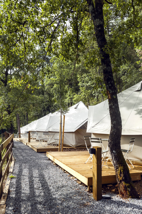 Safari-Zelte der Bell Tent bei Wecamp Pirineos in Spanien mit Holzterrassen und Stühlen im Wald.