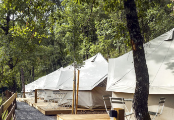 Tiendas safari Bell Tent en Wecamp Pirineos, España, con terrazas de madera y sillas en el bosque.