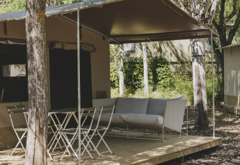 Safari telt kaldet Cottage Family Tent på Wecamp Pirineos i Spanien, med terrasse, stole og sofa i naturen.