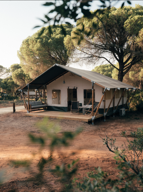 Safari tent in een natuurlijke omgeving omgeven door bomen, met een gezellige veranda en zitruimte.