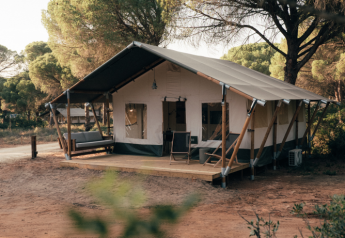 Tenda safari immersa nella natura tra gli alberi, con veranda e zona relax all'esterno.