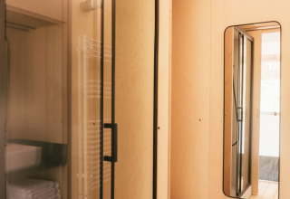 Badkamer in een safaritent met moderne douche, toilet, spiegel en lichte houten wandbekleding.