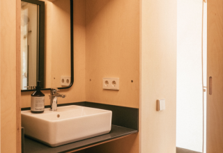 Badkamer in safaritent met wastafel, spiegel, stapels handdoeken en haardrogerzak op houten planken.