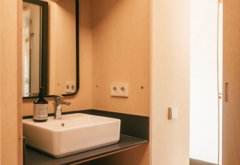 Bagno in tenda safari con lavandino, specchio, asciugamani impilati e sacca per asciugacapelli sugli scaffali.