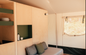 Interieur van een safaritent met licht houten meubels, bank, planken, tafel en raam met zonlicht.