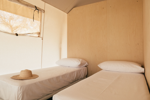 Interieur van een safaritent met twee eenpersoonsbedden en een strohoed, Lodge Family, Wecamp Cádiz, Spanje.
