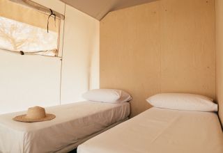 Interieur van een safaritent met twee eenpersoonsbedden en een strohoed, Lodge Family, Wecamp Cádiz, Spanje.