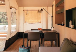 Interior view of a safari tent featuring a wood floor, sofa, dining table, and open kitchenette in natural light.