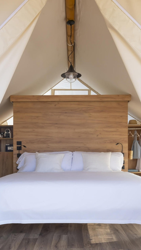 Cozy bed with white bedding inside a safari tent, Glamping Couple, Wecamp Cádiz, Spain.
