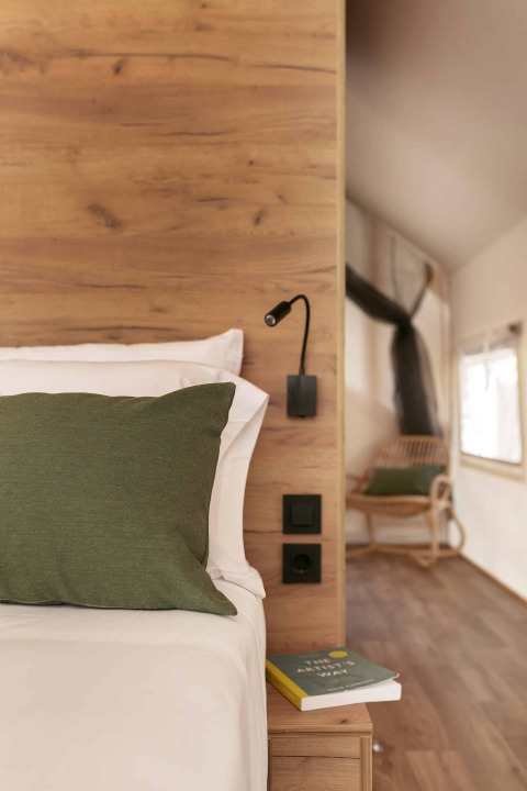 Interieur van een Glamping Comfort safaritent bij Wecamp Cádiz met houten bed, groen kussen en boek.