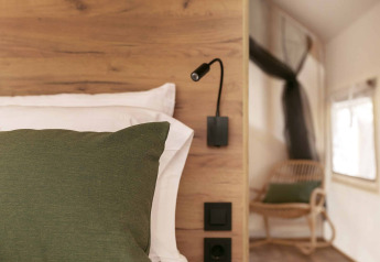 Interno della tenda safari Glamping Comfort presso Wecamp Cádiz con letto in legno, cuscino verde e libro.