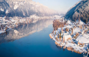 A panoramic winter view of a lake with snowy mountains, cozy cabins, and a small town at the shoreline.