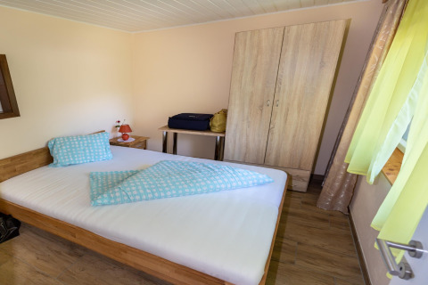 Soveværelse i Blasge Bungalow 1, Østrig, med dobbeltseng, tøjskab, bord og grønne gardiner.