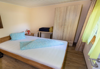 Soveværelse i Blasge Bungalow 1, Østrig, med dobbeltseng, tøjskab, bord og grønne gardiner.