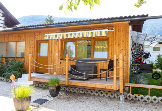 Træhytte med veranda, havemøbler og cykler under halvtag ved Blasge Bungalow 1 i Østrig, omgivet af bjerge.