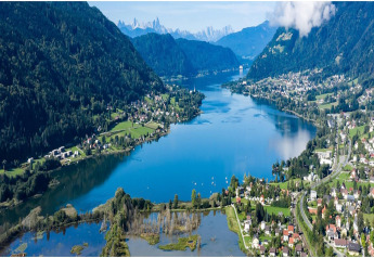 Stunning lake and mountain valley view from a cabin, with villages and lush landscape on a bright day.