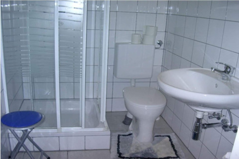 Lille badeværelse i Blasge Bungalow 1 med brusekabine, toilet, håndvask og blå skammel i Østrig.