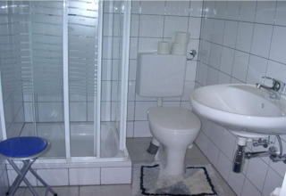 Lille badeværelse i Blasge Bungalow 1 med brusekabine, toilet, håndvask og blå skammel i Østrig.