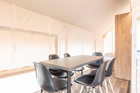 Zona pranzo luminosa con sei sedie nere e un tavolo dentro una tenda safari a Chalets & Glamping Nassfeld 5, Austria.