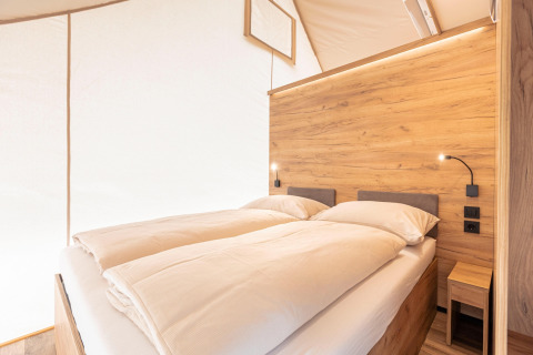 Zona notte moderna in tenda safari ai Chalets & Glamping Nassfeld 5 in Austria, pannelli in legno e luce calda.
