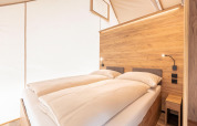 Moderne slaapruimte in safaritent bij Chalets & Glamping Nassfeld 5 in Oostenrijk, houten panelen en sfeerverlichting.