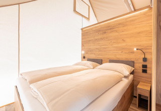 Zona notte moderna in tenda safari ai Chalets & Glamping Nassfeld 5 in Austria, pannelli in legno e luce calda.