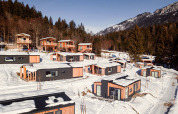 Glamping accommodatie met moderne houten hutten in een besneeuwd berglandschap omringd door dennenbomen.