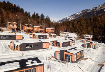 Glamping accommodatie met moderne houten hutten in een besneeuwd berglandschap omringd door dennenbomen.