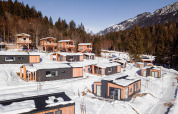 Glamping accommodatie met moderne houten hutten in een besneeuwd berglandschap omringd door dennenbomen.