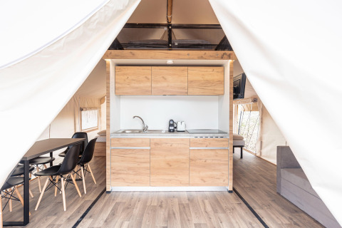 Interno di una tenda safari di lusso con cucina moderna in legno, zona pranzo e letto a Nassfeld, Austria.