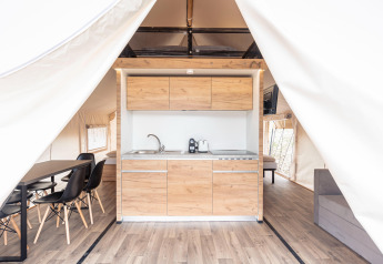 Interieur van een luxe safaritent met moderne houten keuken, eettafel en slaapruimte in Nassfeld, Oostenrijk.
