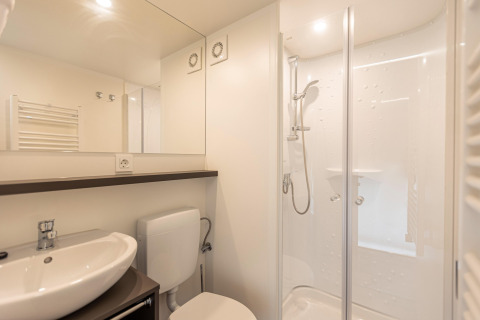 Bagno moderno in una tenda safari con doccia, lavabo, WC e grande specchio sotto luci a soffitto.