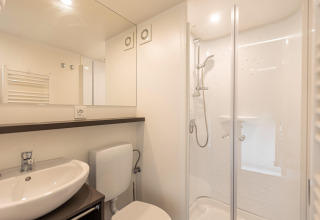 Bagno moderno in una tenda safari con doccia, lavabo, WC e grande specchio sotto luci a soffitto.