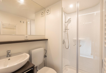 Moderne badkamer in een safaritent met douche, wastafel, toilet en grote spiegel onder plafondverlichting.
