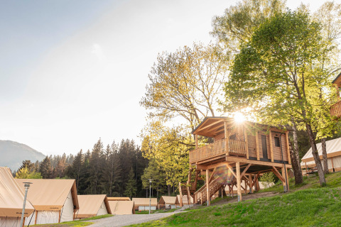 Il sole illumina una casa sull’albero in legno e tende lussuose in un moderno campeggio glamping.