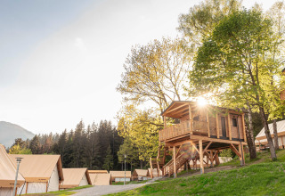 Il sole illumina una casa sull’albero in legno e tende lussuose in un moderno campeggio glamping.