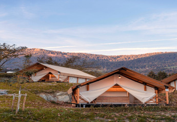 Glamping-Zelte mit Holzrahmen in malerischer Berglandschaft unter klarem blauem Himmel am Abend.