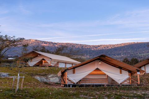 Tende glamping con struttura in legno immerse in un paesaggio montano sotto un cielo azzurro e limpido.