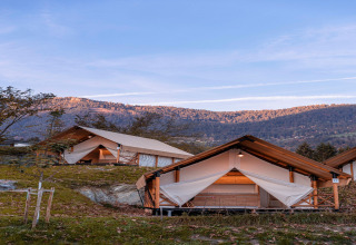 Tende glamping con struttura in legno immerse in un paesaggio montano sotto un cielo azzurro e limpido.