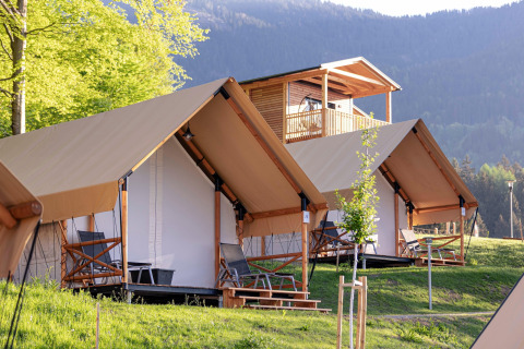 Tende safari e chalet in legno al Chalets & Glamping Nassfeld, immersi in una cornice montana verde.