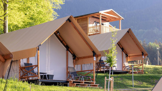 Tende safari e chalet in legno al Chalets & Glamping Nassfeld, immersi in una cornice montana verde.