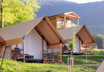 Safari-tenten en houten chalets bij Chalets & Glamping Nassfeld, midden in het groene berglandschap.