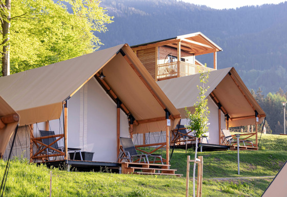 Tende safari e chalet in legno al Chalets & Glamping Nassfeld, immersi in una cornice montana verde.